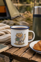 Emaille-Tasse mit blauem Rand und Katzenmotiv beim Camping mit Thermosflasche, Buch und Croissant